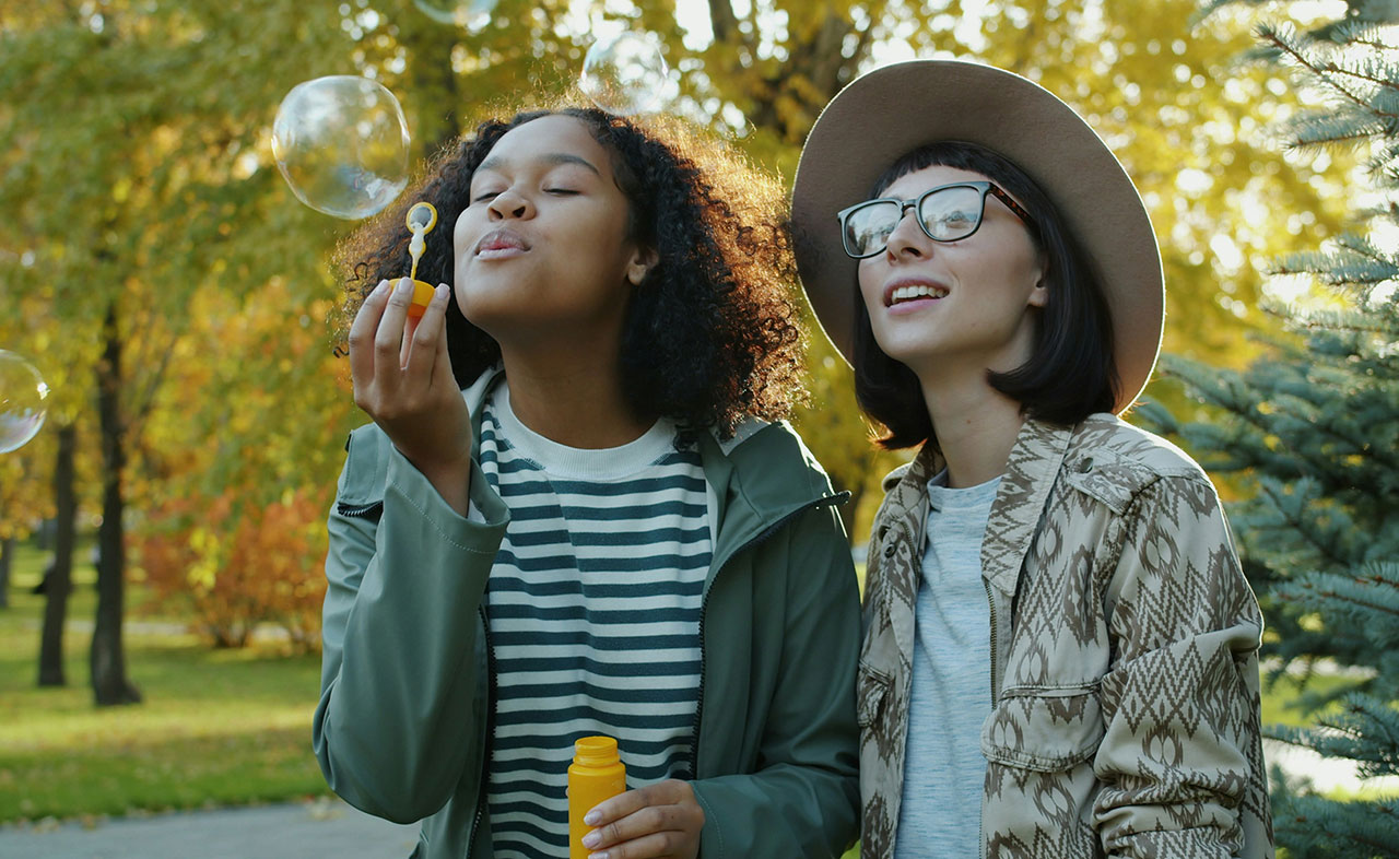 A photo of two teenage girls blowing bubbles in a park.