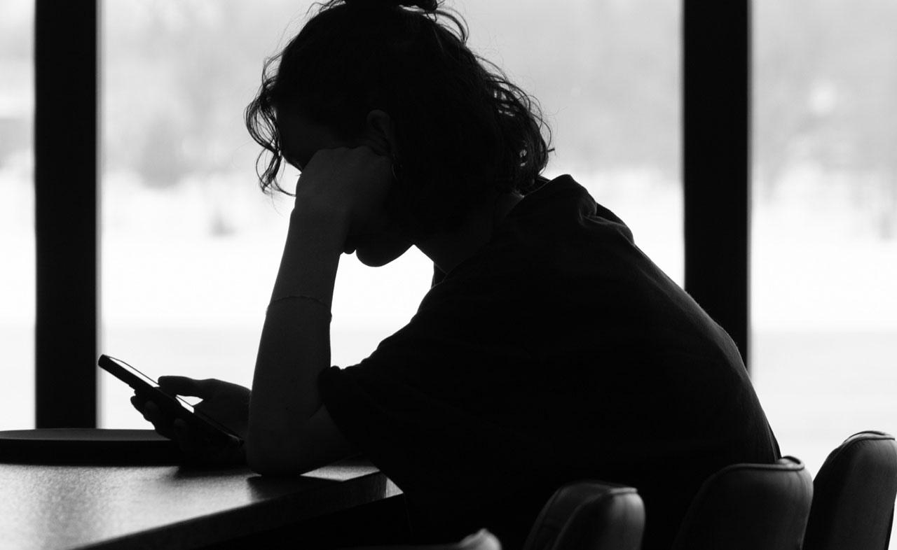 A black and white photo of a teenager looking at their phone.
