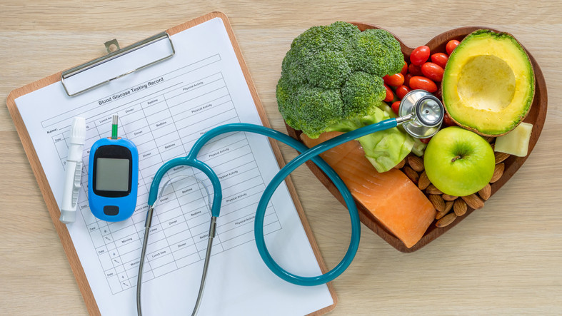 Diabetes monitoring tools and chart, stethoscope, and heart-shaped bowl of healthy foods