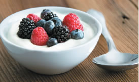 A bowl of yogurt with fresh raspberries, blueberries, and blackberries, with a spoon next to the bowl.