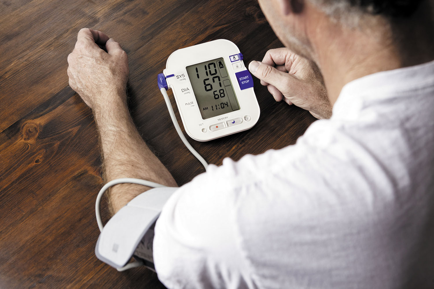 over the shoulder view of a man using a home blood pressure monitoring device