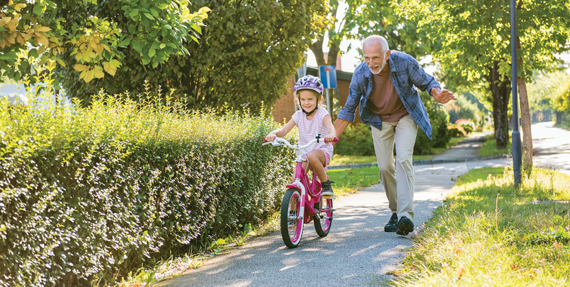 photo of a grandfather helping his granddaughter learn how to ride a bicycle without training wheels on a sidewalk