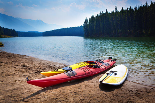 deux kayaks et une planche à pagaie sur la plage adjacente à un lac