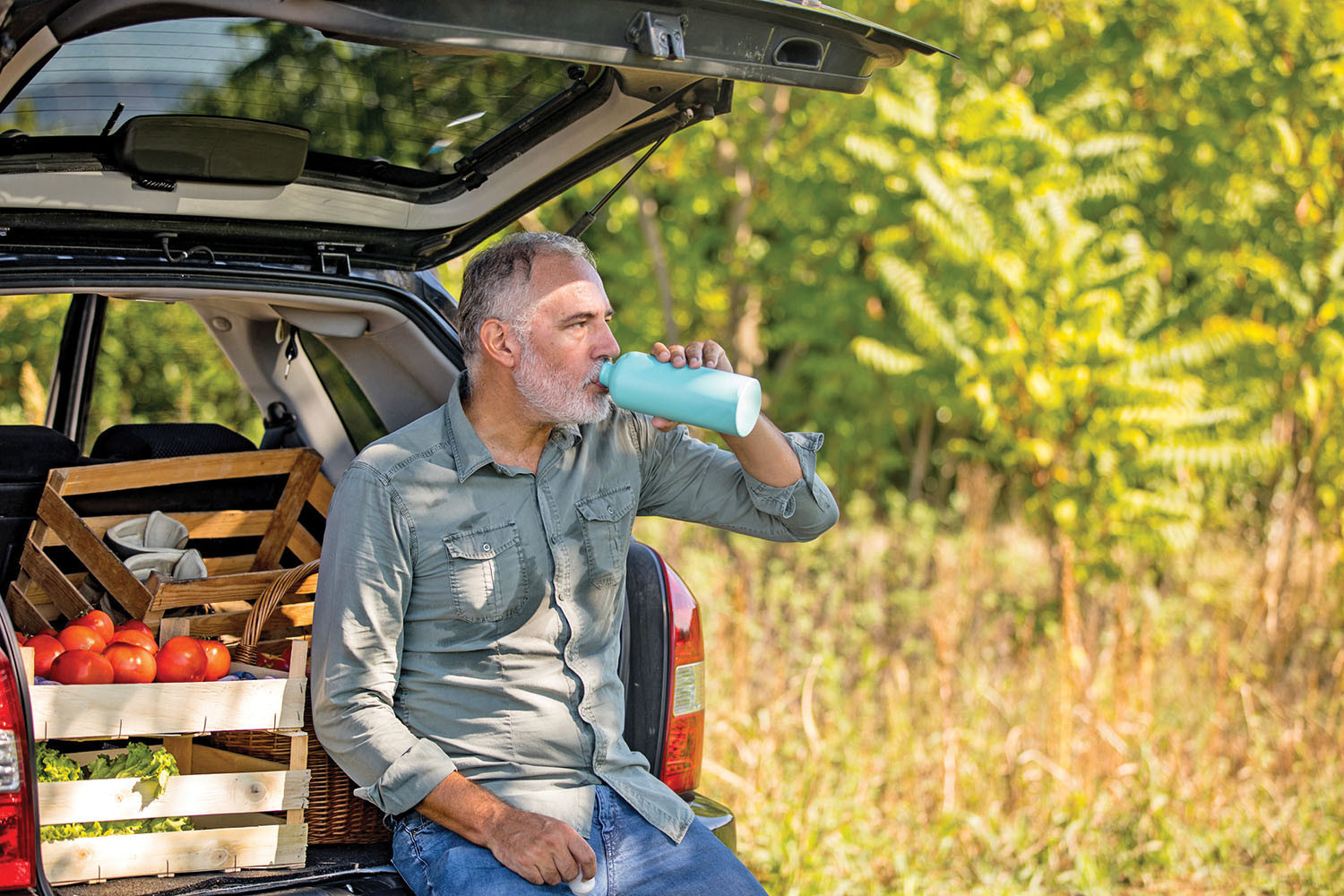 photo d'un homme plus âgé qui boit de l'eau assis à l'arrière d'une voiture