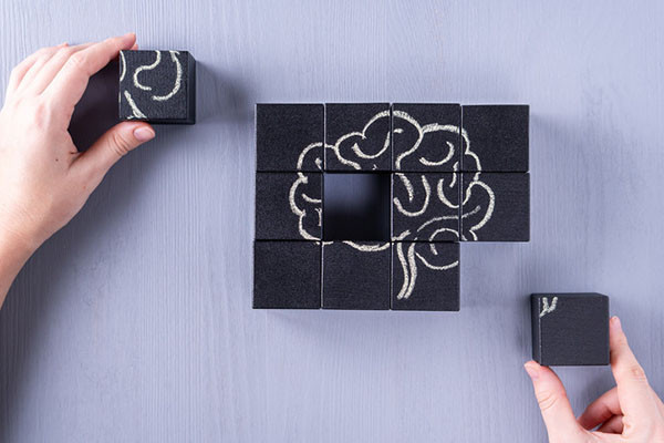 photo showing an overhead view of hands assembling a puzzle containing a drawing of a brain