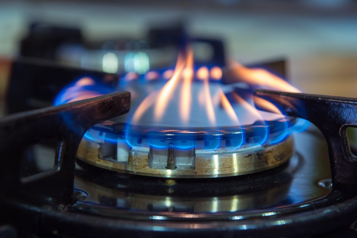 A gas stove burner with blue and yellowish flames;  another burner in the background is blurred