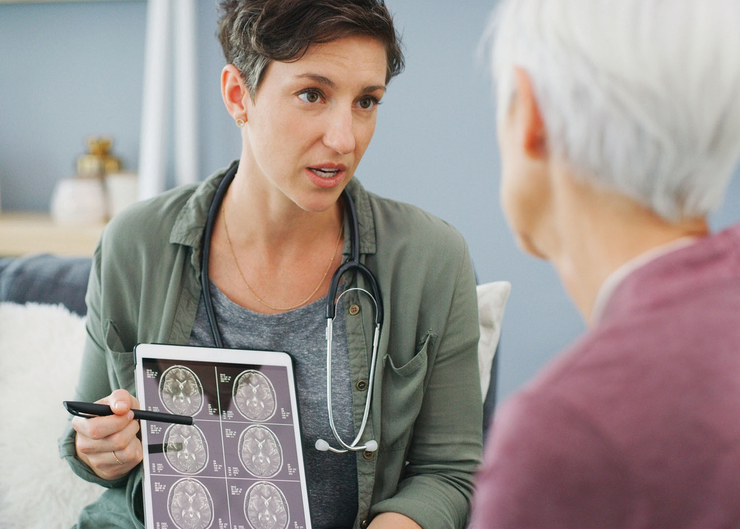 Photo of a doctor holding a tablet with MRI images and talking to a patient