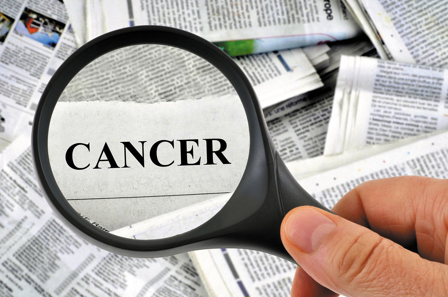 photo of a hand holding a magnifying glass over a disheveled pile of papers, highlighting the word cancer