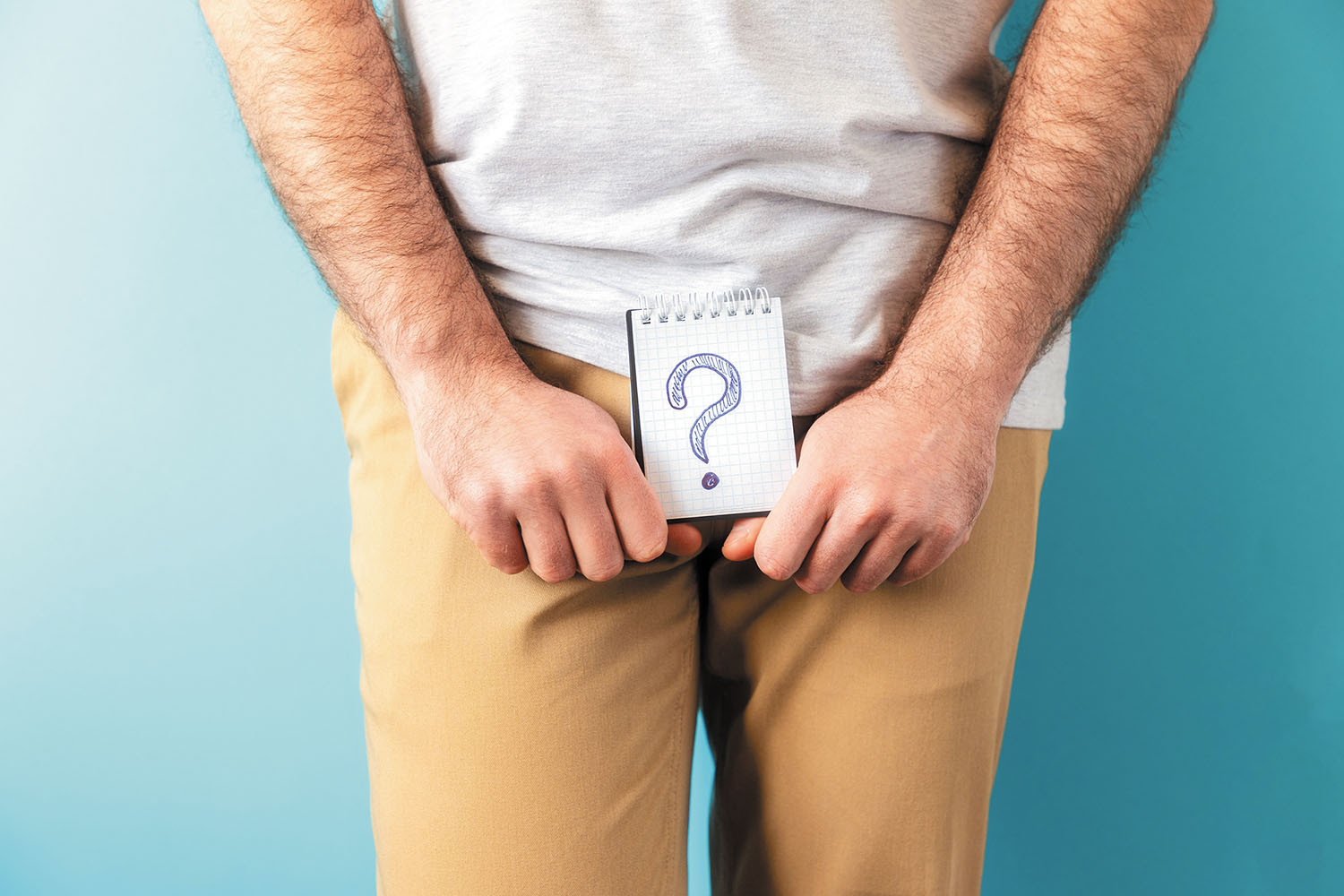 cropped photo of the midsection of a man who is holding a notepad in front of his groin area with a question mark drawn on it