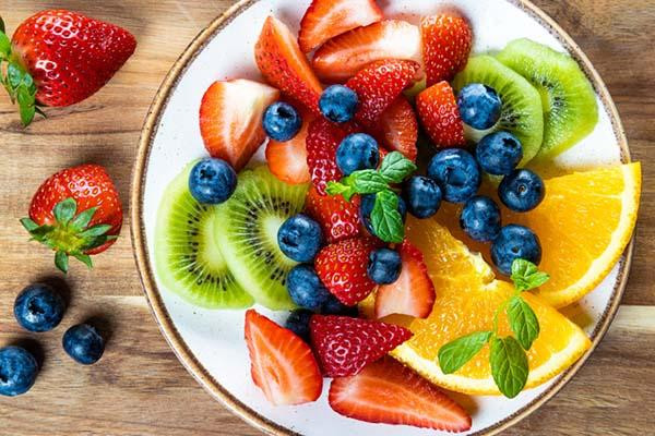 Overhead close-up of a plate of assorted fresh fruit including sliced strawberries, kiwi, blueberries, and oranges.