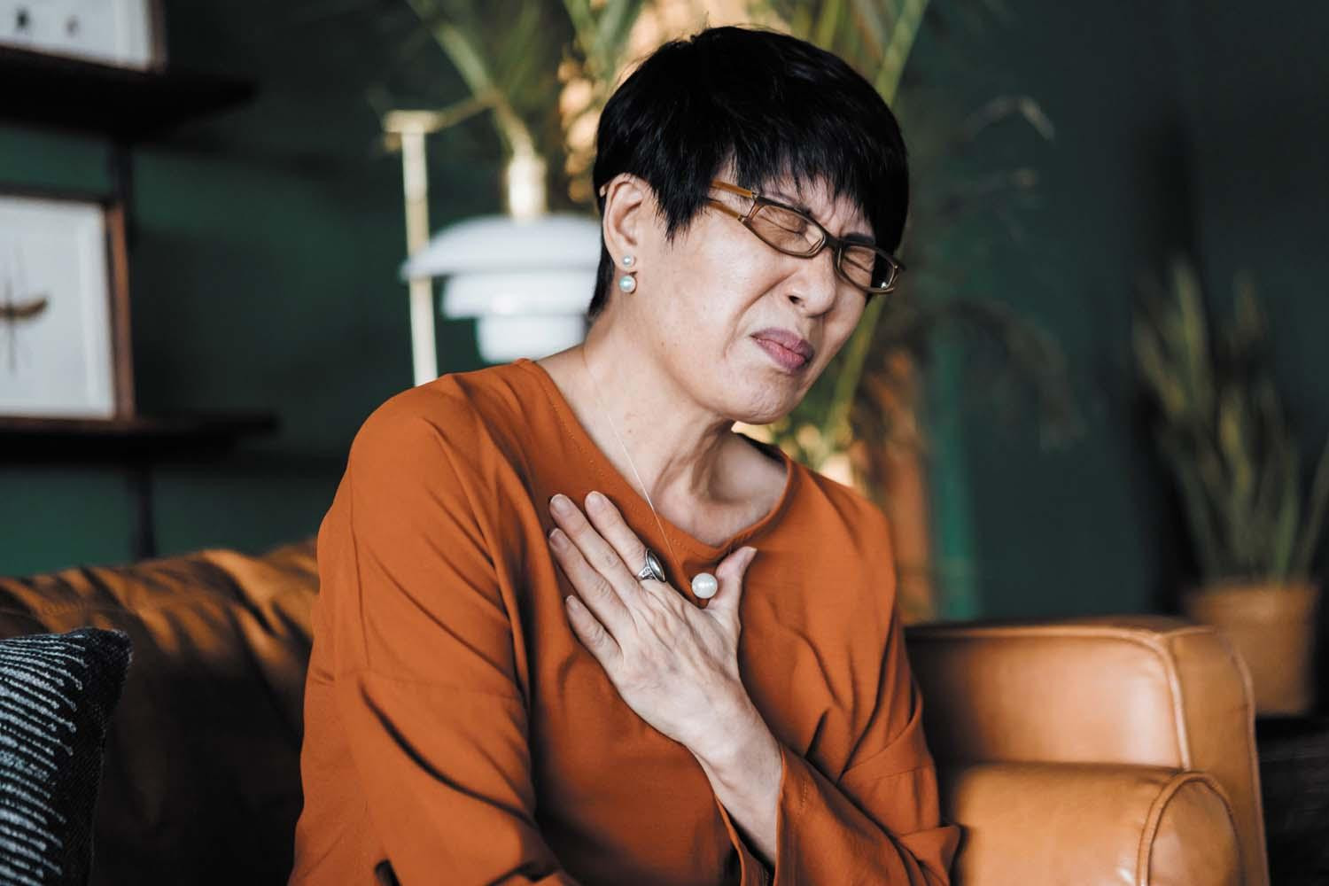 A woman with a look of discomfort, suffering from a stomach issue, holds a hand to her upper chest.