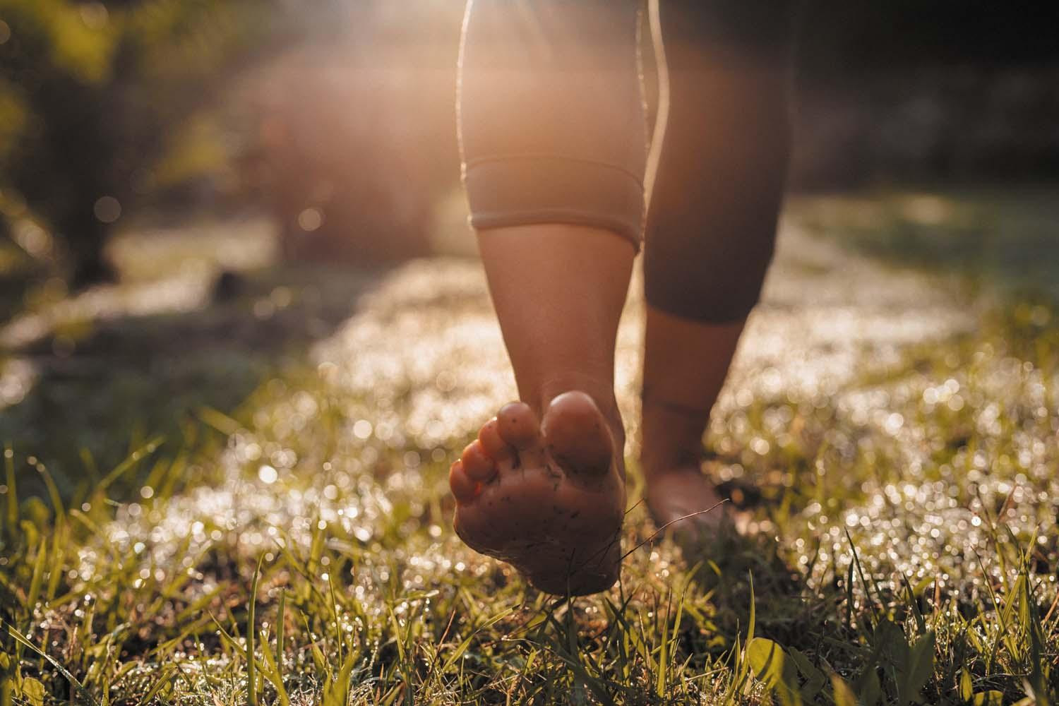 Close-up of a person's bare feet and ankles as she walks on a lawn.