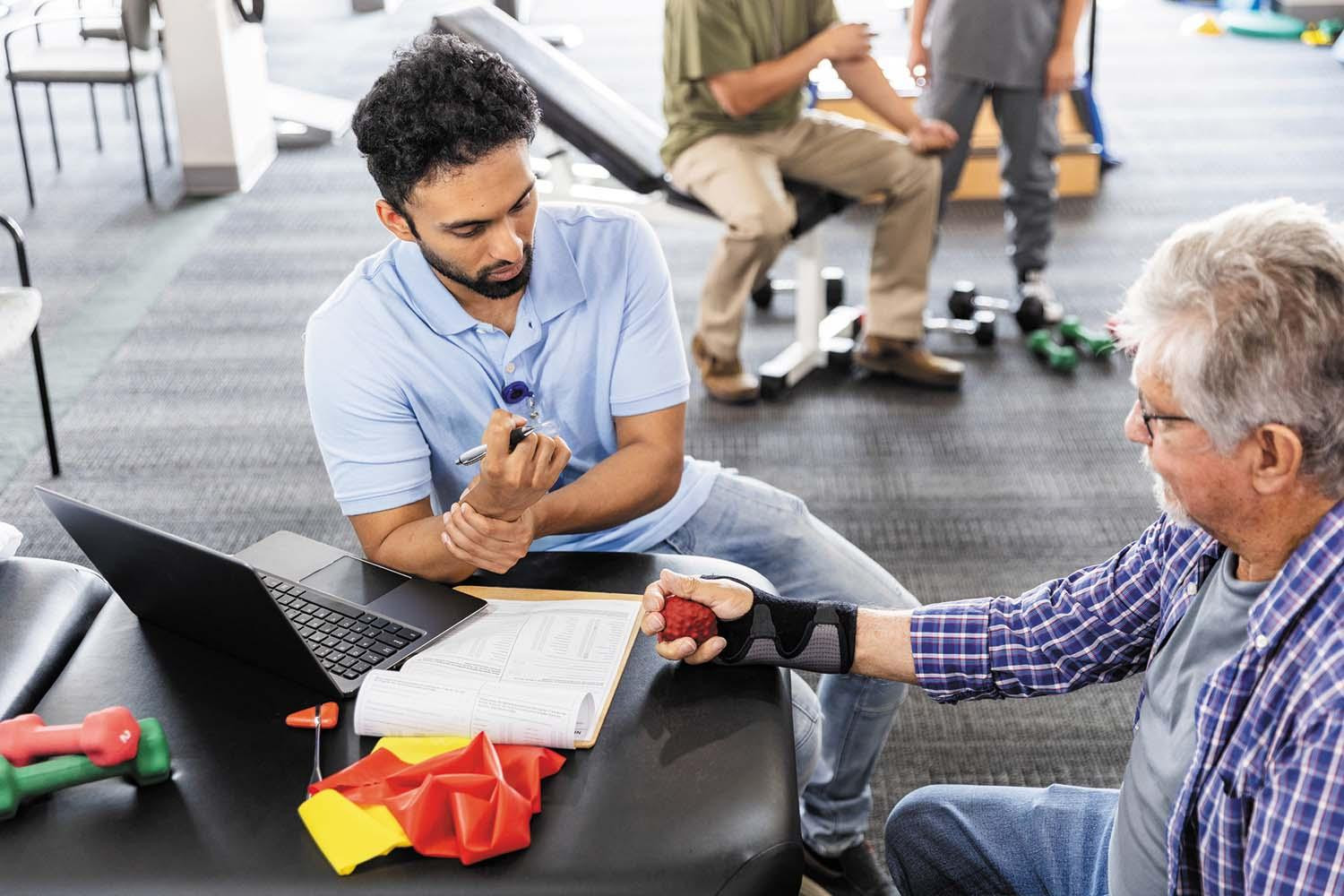 A certified hand therapist shows a person how to do a hand strengthening exercise using a squeeze ball.