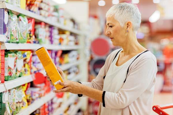 A senior woman reads the label on a food package in a supermarket.
