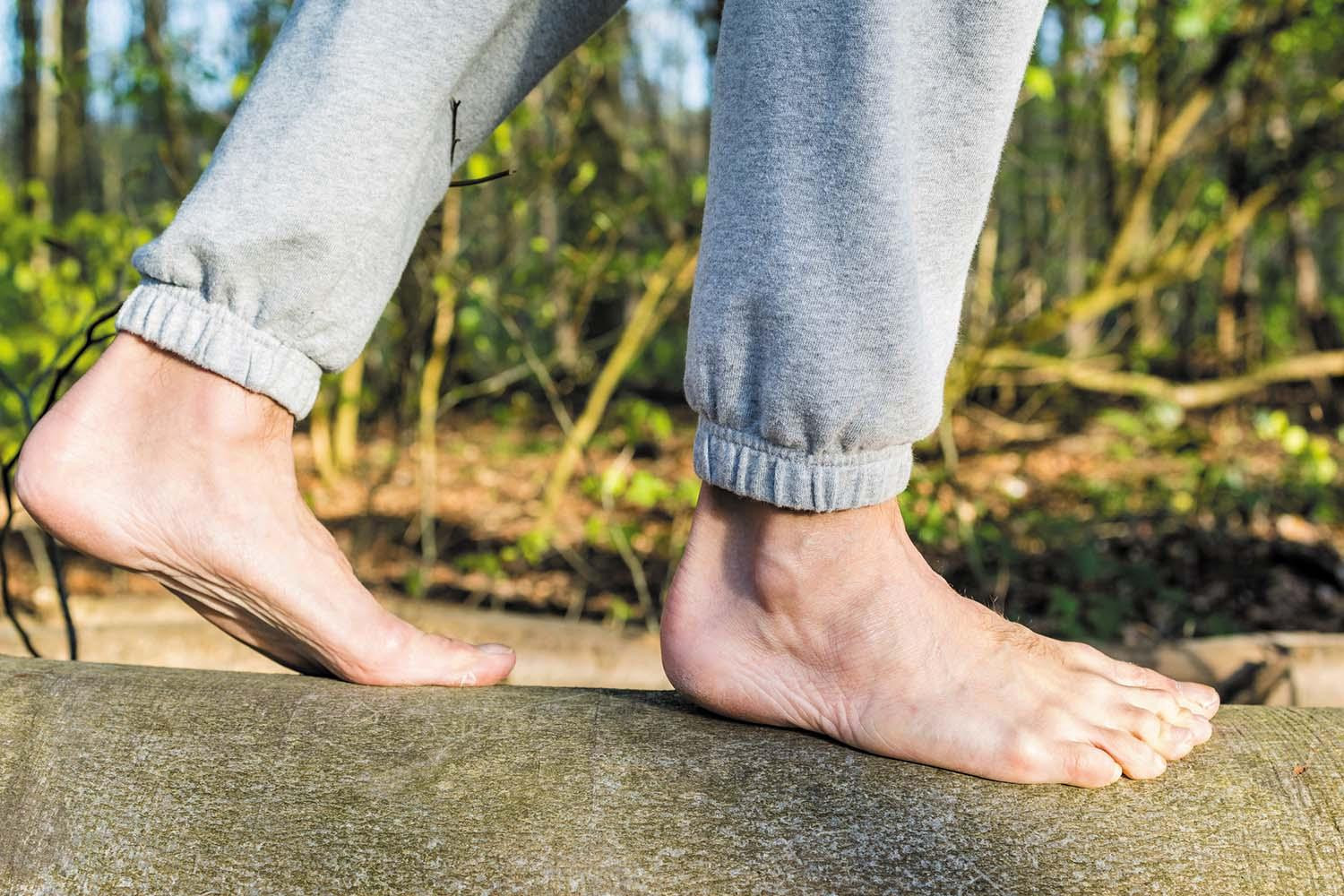 Cropped image showing the legs and feet of a man walking barefoot on a log.