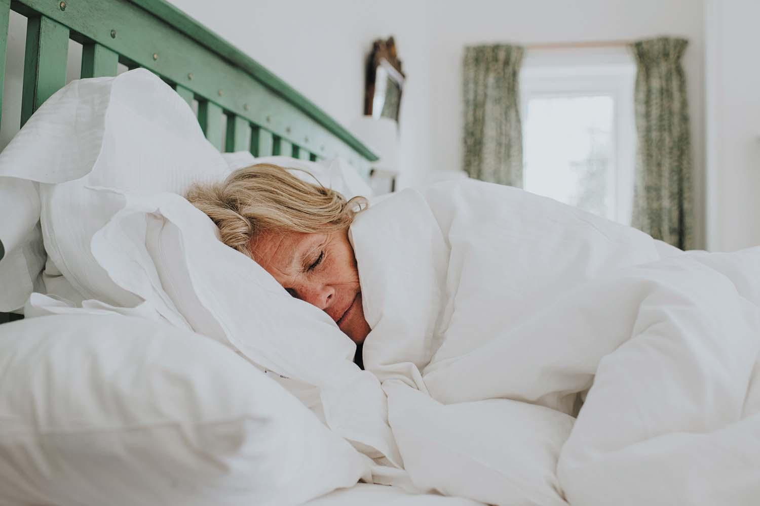 A woman sleeping, snuggled under a comforter.