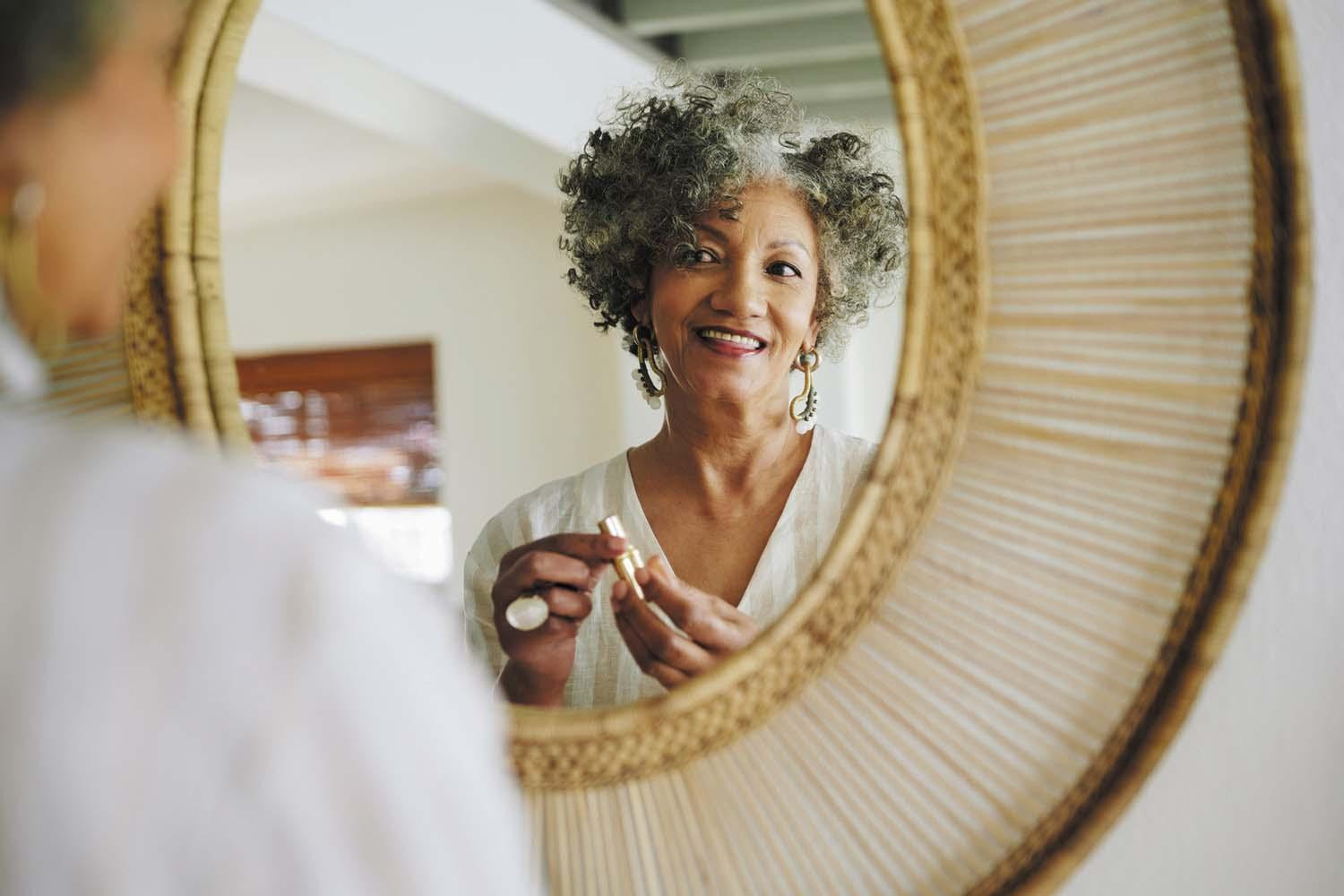 A youthful-looking mature woman looks at herself in a mirror.