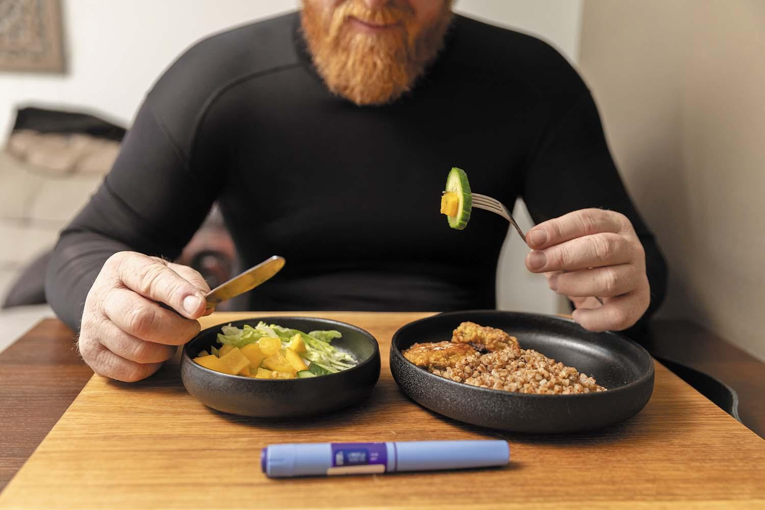 A man eats a meal with a GLP-1 weight loss medication injector on the table in front of his bowl.