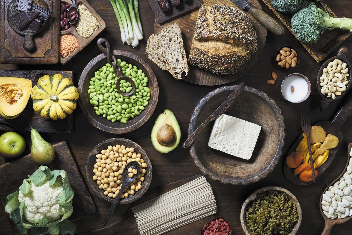 An arrangement of foods viewed from above that provide high-quality carbohydrates, including legumes, whole-grain bread, cauliflower, scallions, nuts, tofu, and more.