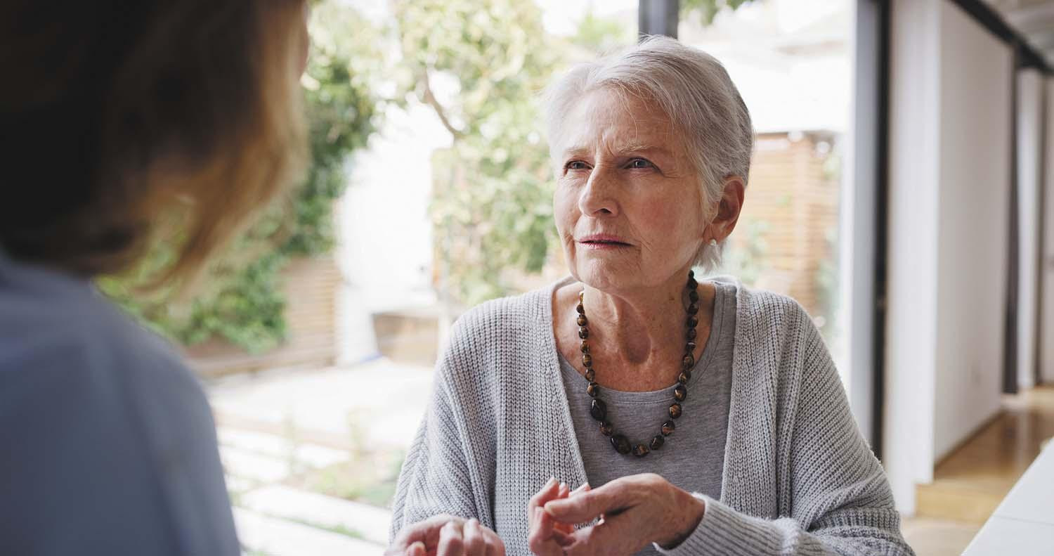 A senior woman looking confused, viewed over the shoulder of another person.