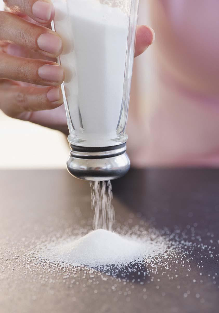 Close-up of a hand holding a glass salt shaker upside down, with the salt streaming out onto and forming a pile.