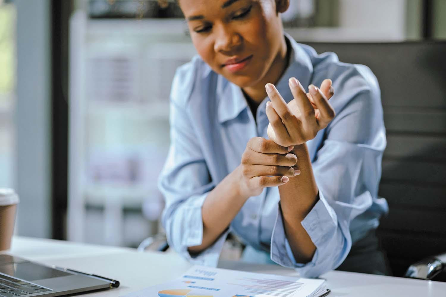 A woman sitting at a desk holds her wrist with her other hand.