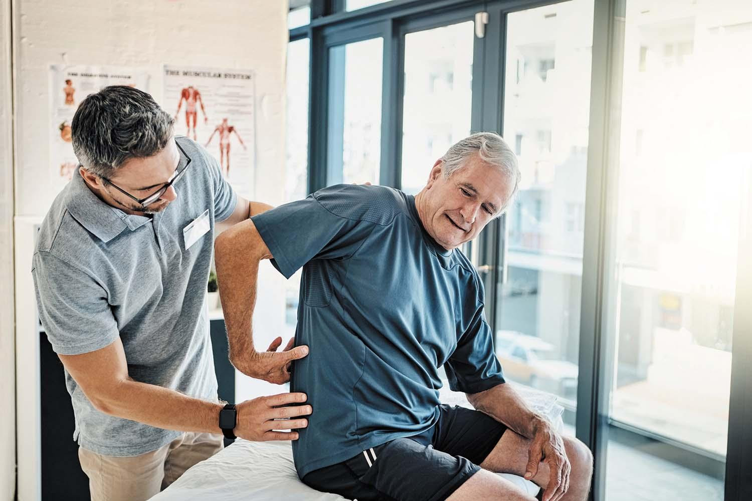 A man in an exam room shows the person examining him where he is having back pain.
