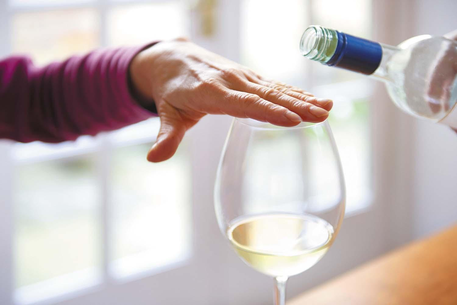 Cropped image showing a man's hand held above a wine glass with a small amount in it, to prevent more from being poured into it.