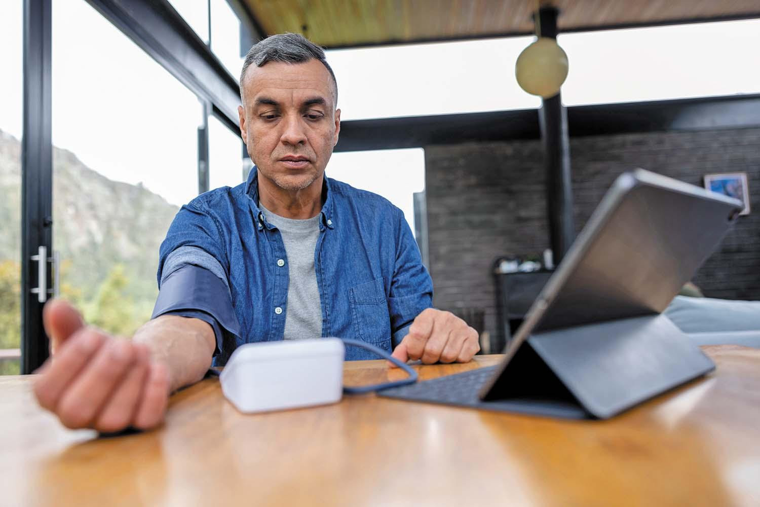 A mature man takes his blood pressure at home, using a personal device connected to his tablet.