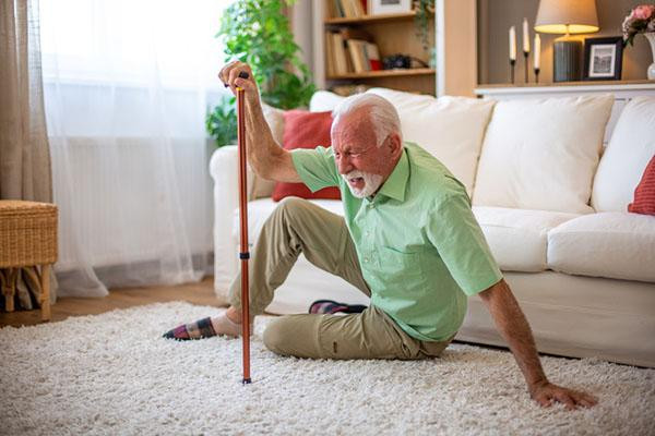 A senior man who has fallen at home and is using his cane to assist in getting back on his feet, with an expression of pain on his face.