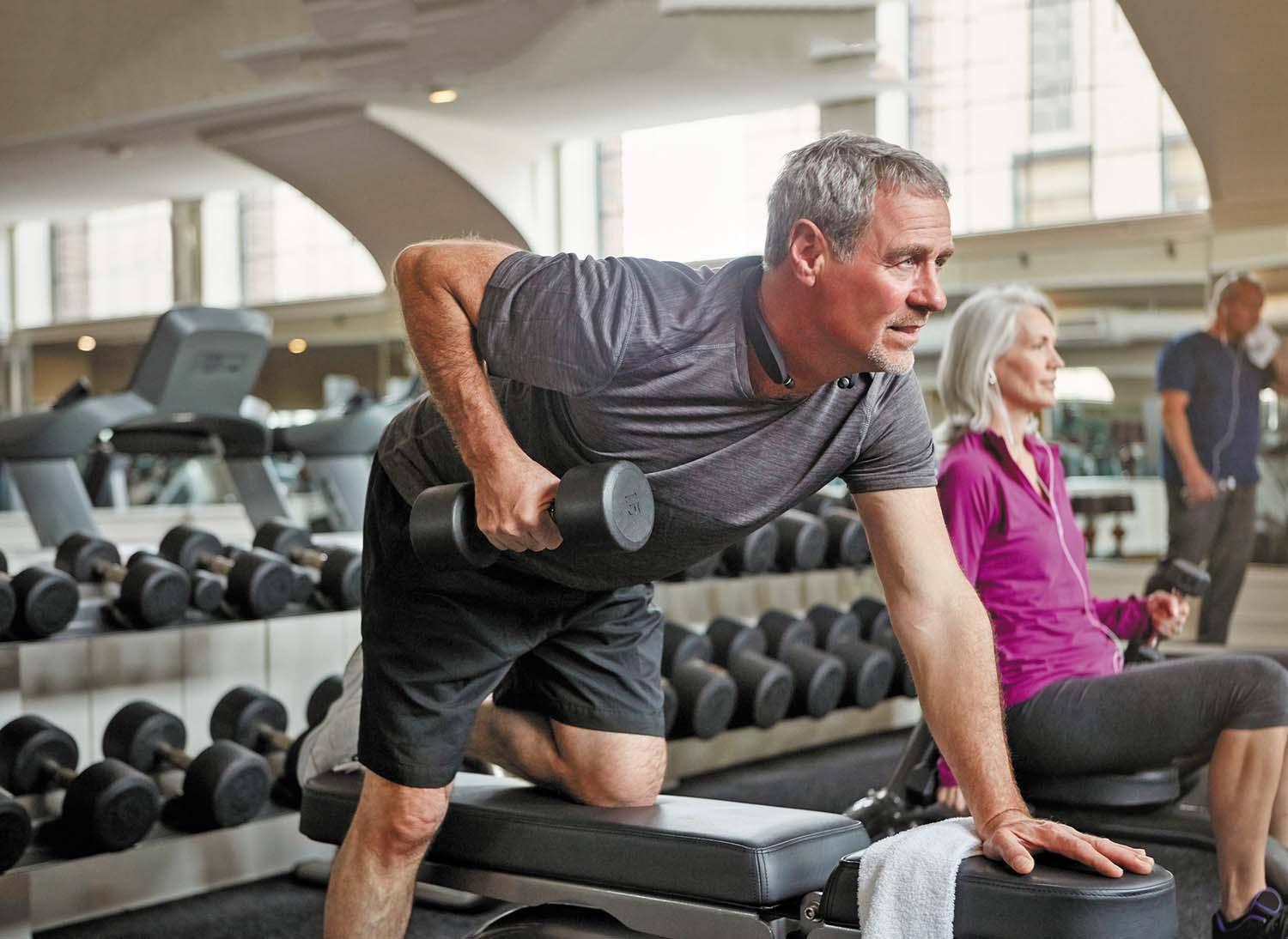 A mature man works out with hand weights in a gym.