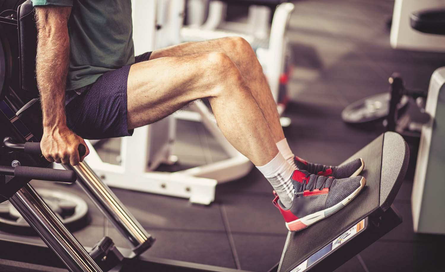 Cropped image showing the torso and legs of a man working out on a leg machine in a gym.