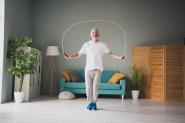 A mature man jumps rope in his living room.