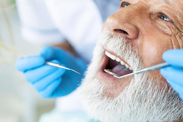 Close-up of a senior man having dental work done; gloved hands are holding a pick and a mirror.