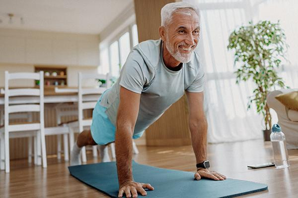 A senior man does push-ups in his home on a yoga mat.