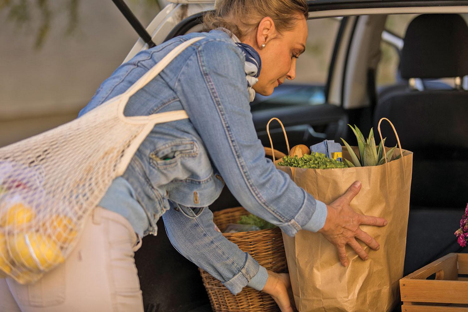 A woman carrying a bag of groceries from the back of a car