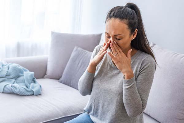 Woman sits on the couch holding her nose from sinusitis.