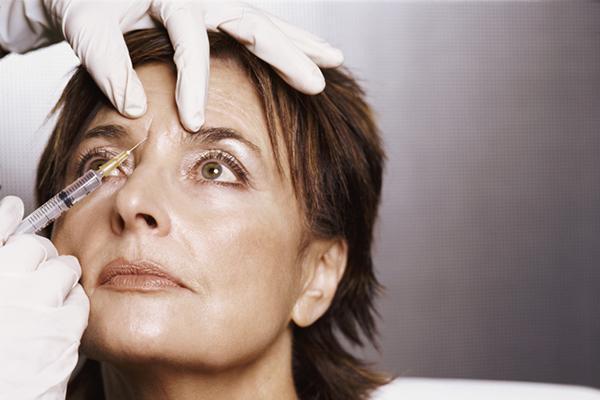 A middle-age woman receives an injection of botulinum toxin in her forehead between her eyes.