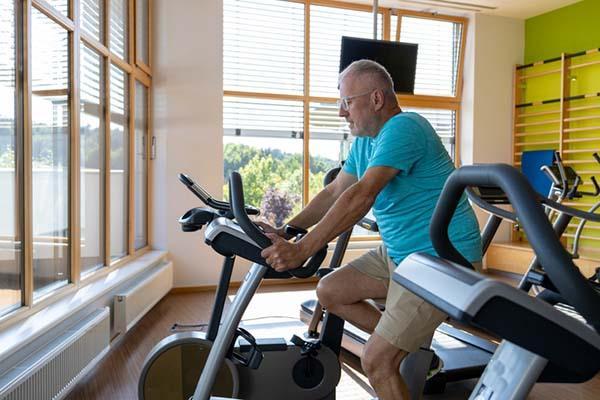 A senior man uses a stationary bicycle in a sunlit room.