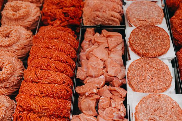 Assorted types of raw meat, some bright red and some more pink, on display in a deli case.