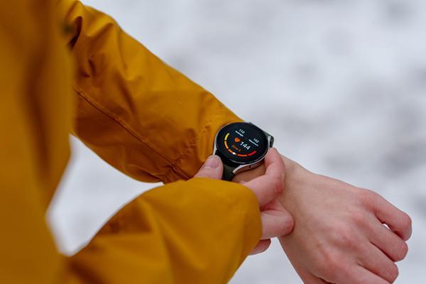 Close-up of the arms and hands of a person checking their heart rate on a smartwatch during a winter workout (snow is visible in the background, out of focus).