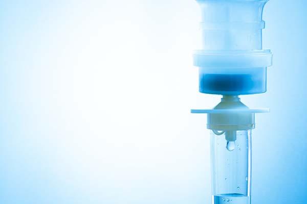 close-up photo of the neck of an intravenous drip bag and the top of the tube attached to it; image has a blue tint