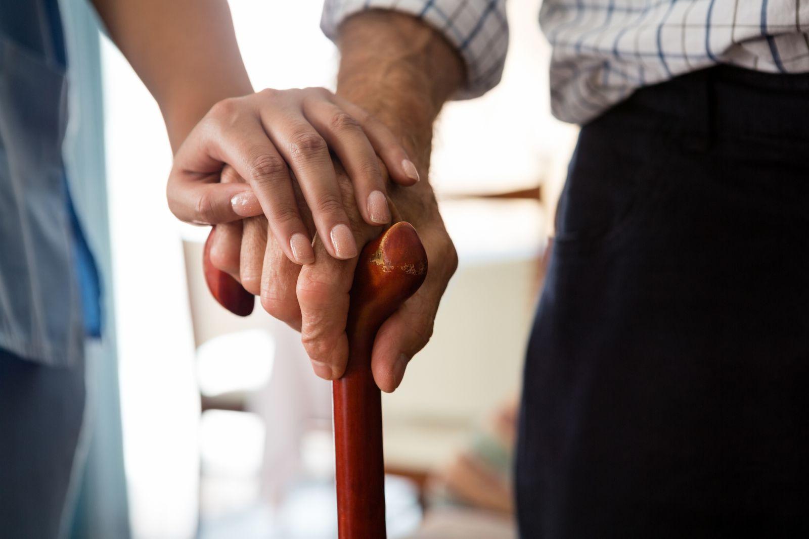 Younger woman putting her hand over an older man's hand on a cane.