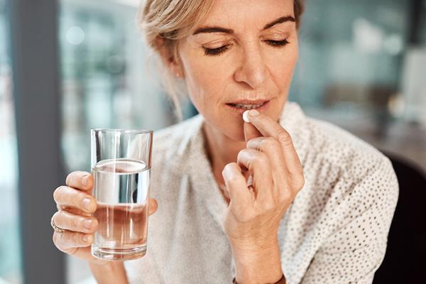 A middle-age woman holds a pill and a glass of water, she is about to put the pill into her mouth.