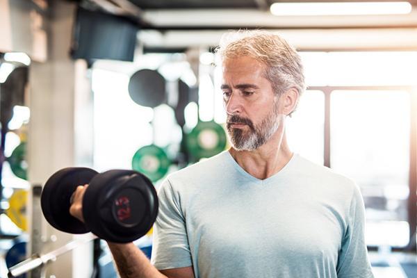 A mature man does curls in a gym using hand weights.