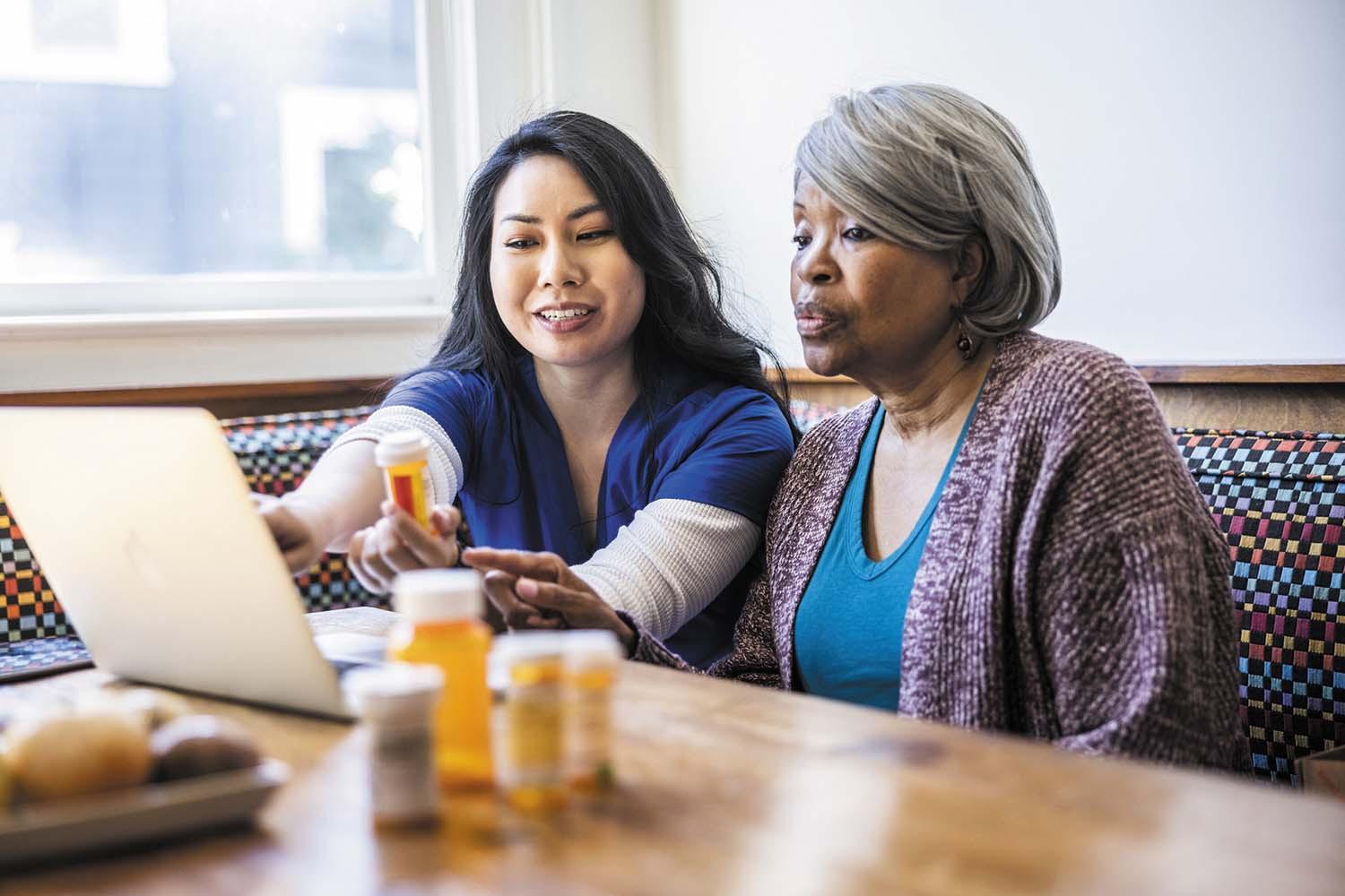 photo of a health professional explaining medications to an older woman; there are several medication bottles on the table in front of them
