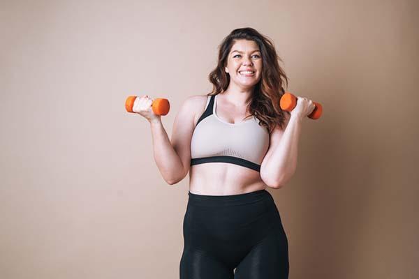 A young woman in workout clothing exercises with dumbbells.