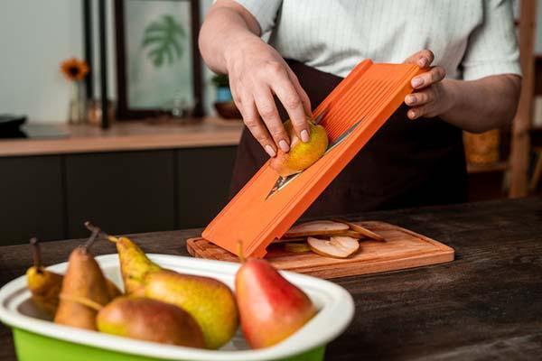 Cropped image of the arms and hands of a woman using a mandoline to slice a pear.