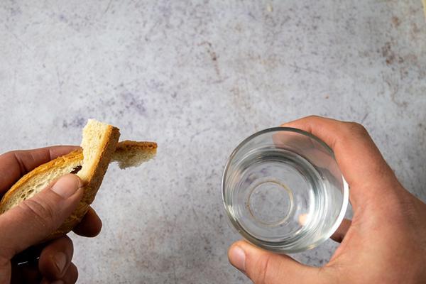Point-of-view shot looking down on hands holding a piece of bread and a glass of water.
