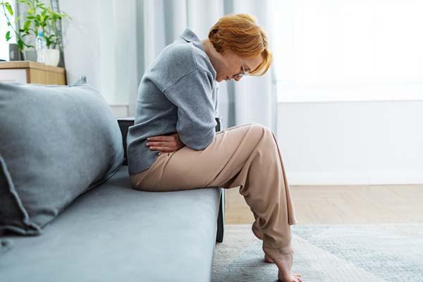 A woman viewed from the side, sitting on a couch with her head down and her arms crossed holding her midsection.